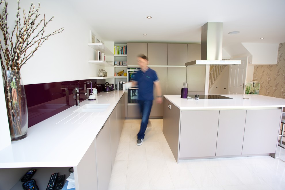 Design ideas for a medium sized contemporary u-shaped kitchen/diner in Hampshire with an integrated sink, flat-panel cabinets, grey cabinets, composite countertops, blue splashback, glass sheet splashback, stainless steel appliances, porcelain flooring and an island.