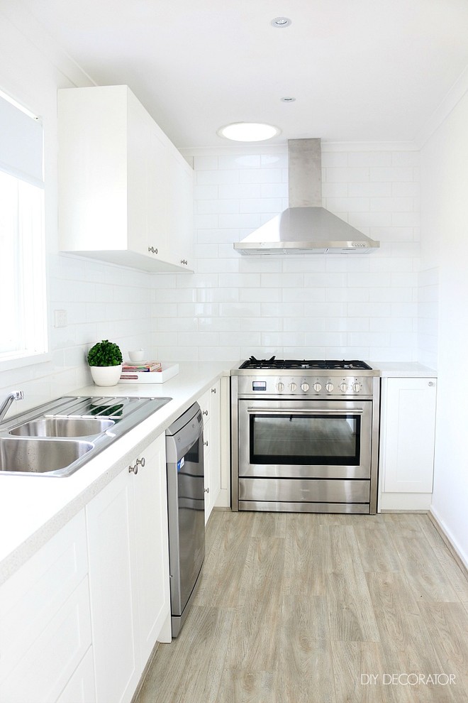 This is an example of a contemporary kitchen in Melbourne with flat-panel cabinets, white cabinets, white splashback, ceramic splashback, stainless steel appliances and light hardwood flooring.