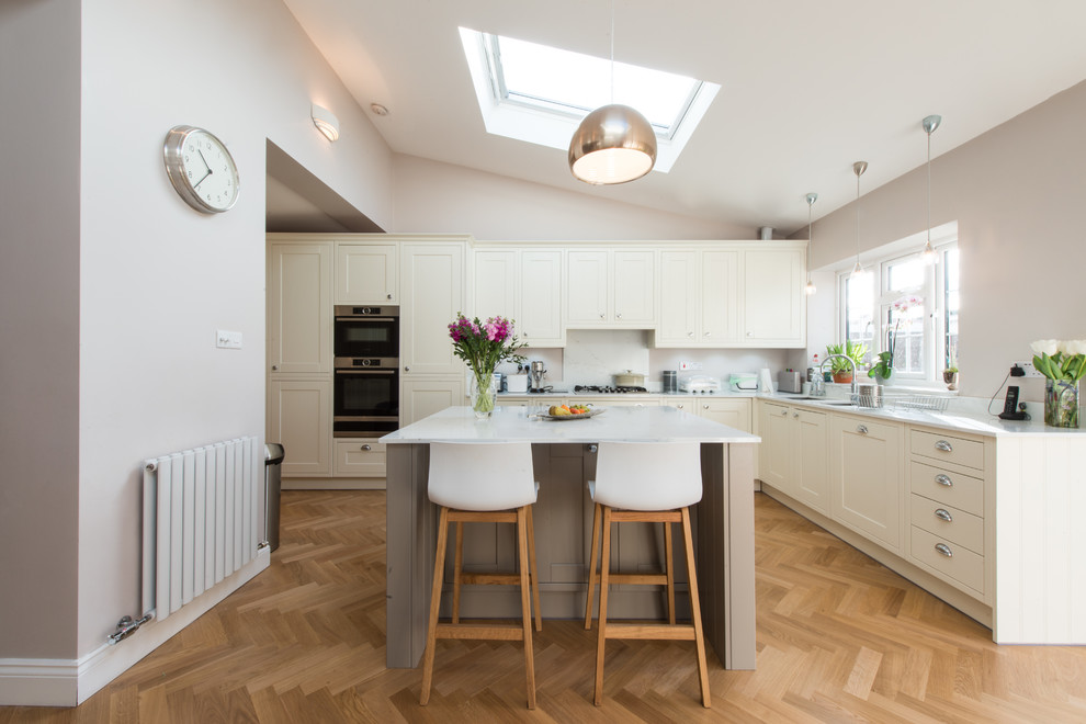 Design ideas for a medium sized traditional l-shaped open plan kitchen in London with a built-in sink, shaker cabinets, quartz worktops, stainless steel appliances, light hardwood flooring, an island and white worktops.