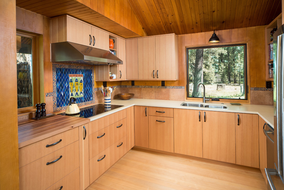 Cette image montre une cuisine design en U et bois clair avec un plan de travail en quartz modifié, un évier 2 bacs, un placard à porte plane, un électroménager en acier inoxydable et une crédence bleue.