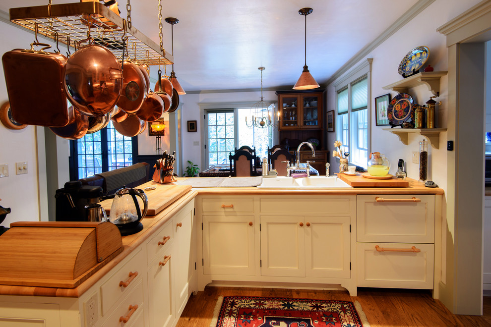 Lantlig inredning av ett mellanstort kök, med en dubbel diskho, luckor med profilerade fronter, vita skåp, träbänkskiva, mellanmörkt trägolv och en halv köksö