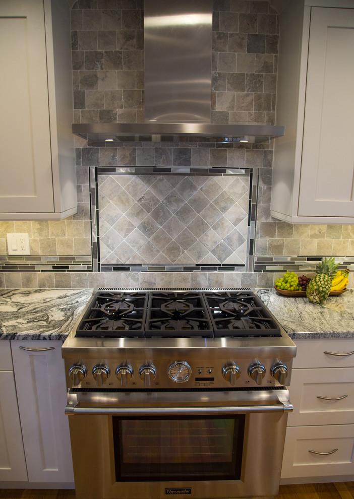 Bild på ett mellanstort funkis kök, med en enkel diskho, skåp i shakerstil, vita skåp, granitbänkskiva, grönt stänkskydd, stänkskydd i porslinskakel, rostfria vitvaror, mellanmörkt trägolv och en köksö