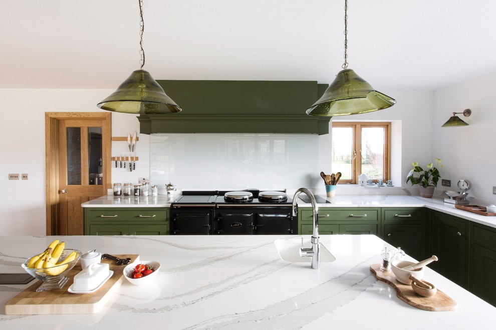 Inredning av ett lantligt stort vit vitt kök, med en rustik diskho, luckor med profilerade fronter, gröna skåp, bänkskiva i kvartsit, glaspanel som stänkskydd, svarta vitvaror, mellanmörkt trägolv, en köksö och brunt golv