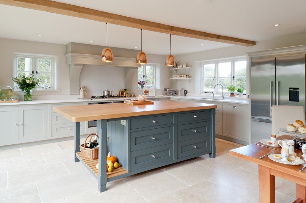 Photo of a large rural l-shaped kitchen/diner in Kent with flat-panel cabinets, blue cabinets, composite countertops, stainless steel appliances, limestone flooring, an island and glass sheet splashback.