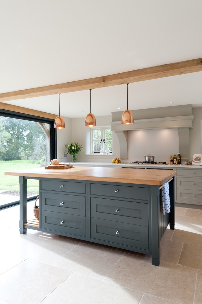 This is an example of a large farmhouse l-shaped kitchen/diner in Kent with flat-panel cabinets, blue cabinets, composite countertops, white splashback, stone tiled splashback, stainless steel appliances, limestone flooring and an island.