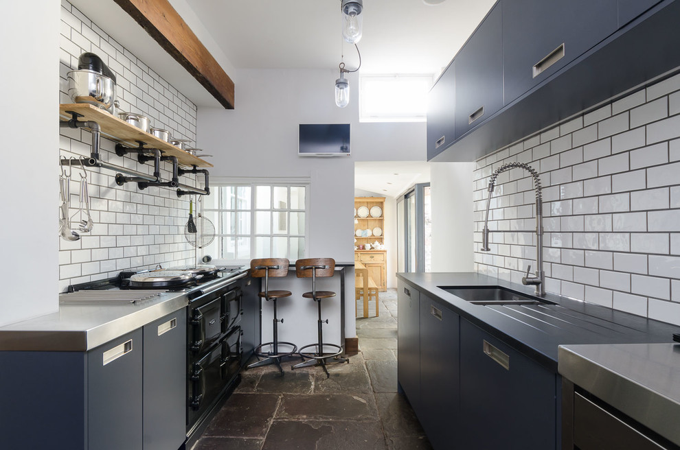 Industrial galley kitchen in Other with a double-bowl sink, flat-panel cabinets, blue cabinets, stainless steel worktops, white splashback, metro tiled splashback, black appliances and no island.