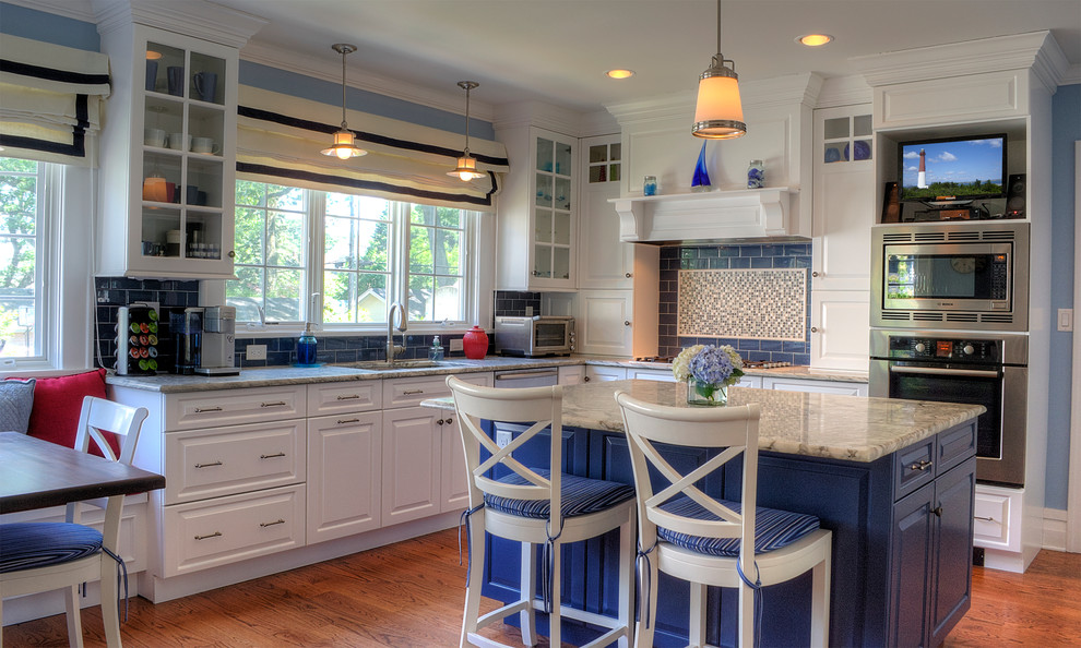 Klassisk inredning av ett kök, med luckor med upphöjd panel, vita skåp, blått stänkskydd, stänkskydd i tunnelbanekakel, rostfria vitvaror och marmorbänkskiva