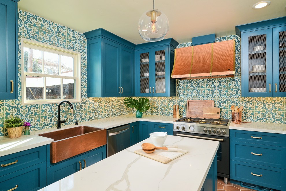 Klassische Küche in U-Form mit Landhausspüle, Schrankfronten mit vertiefter Füllung, blauen Schränken, bunter Rückwand, Küchengeräten aus Edelstahl, Kücheninsel, braunem Boden und weißer Arbeitsplatte in Sonstige
