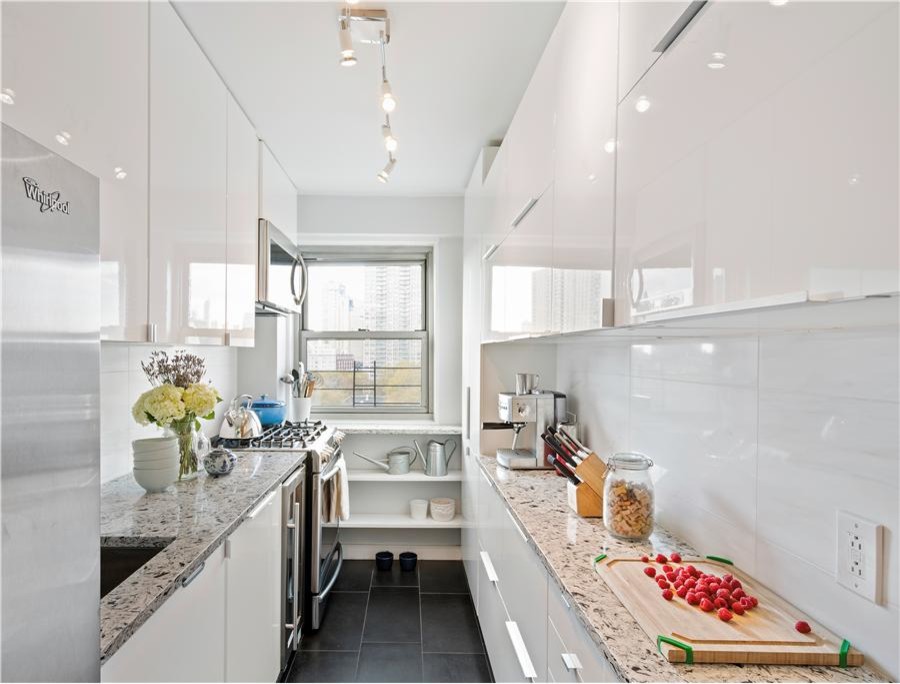 Inspiration for a small transitional galley porcelain tile enclosed kitchen remodel in New York with an undermount sink, flat-panel cabinets, white cabinets, quartzite countertops, white backsplash, stone tile backsplash and stainless steel appliances
