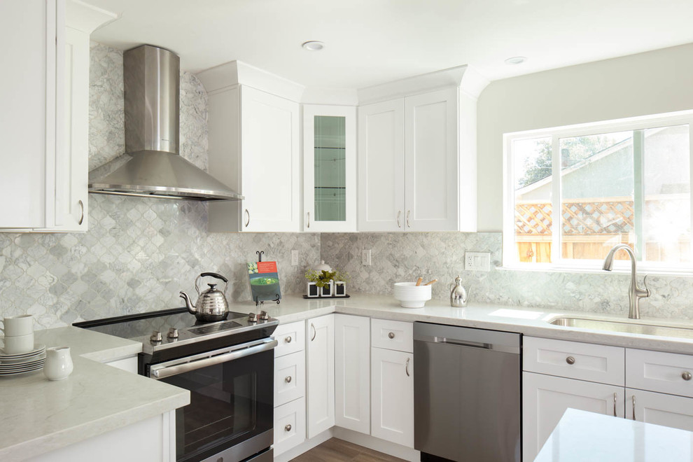 Amerikansk inredning av ett mellanstort vit vitt kök, med en undermonterad diskho, skåp i shakerstil, vita skåp, bänkskiva i kvarts, grått stänkskydd, stänkskydd i marmor, rostfria vitvaror, laminatgolv, en köksö och brunt golv