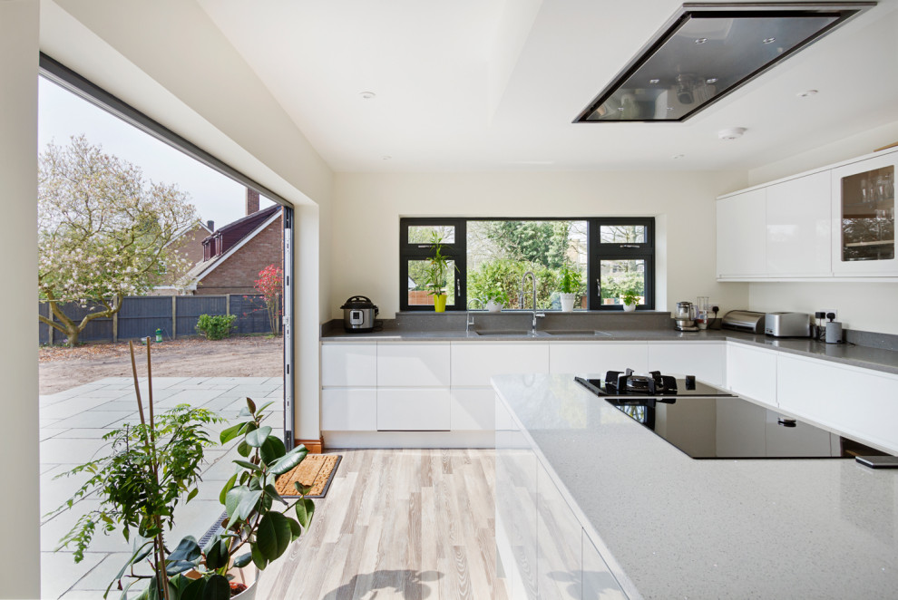 This is an example of a medium sized contemporary l-shaped open plan kitchen in West Midlands with flat-panel cabinets, white cabinets, grey splashback, integrated appliances, laminate floors, an island, grey floors and grey worktops.