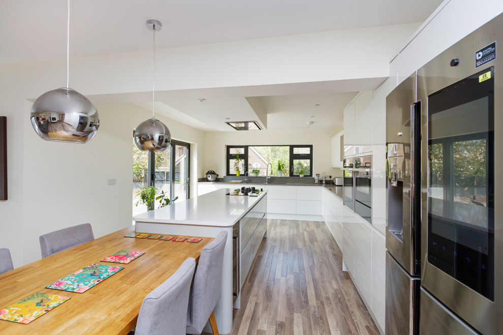 Design ideas for a medium sized contemporary l-shaped open plan kitchen in West Midlands with a built-in sink, flat-panel cabinets, white cabinets, grey splashback, integrated appliances, laminate floors, an island, grey floors and grey worktops.