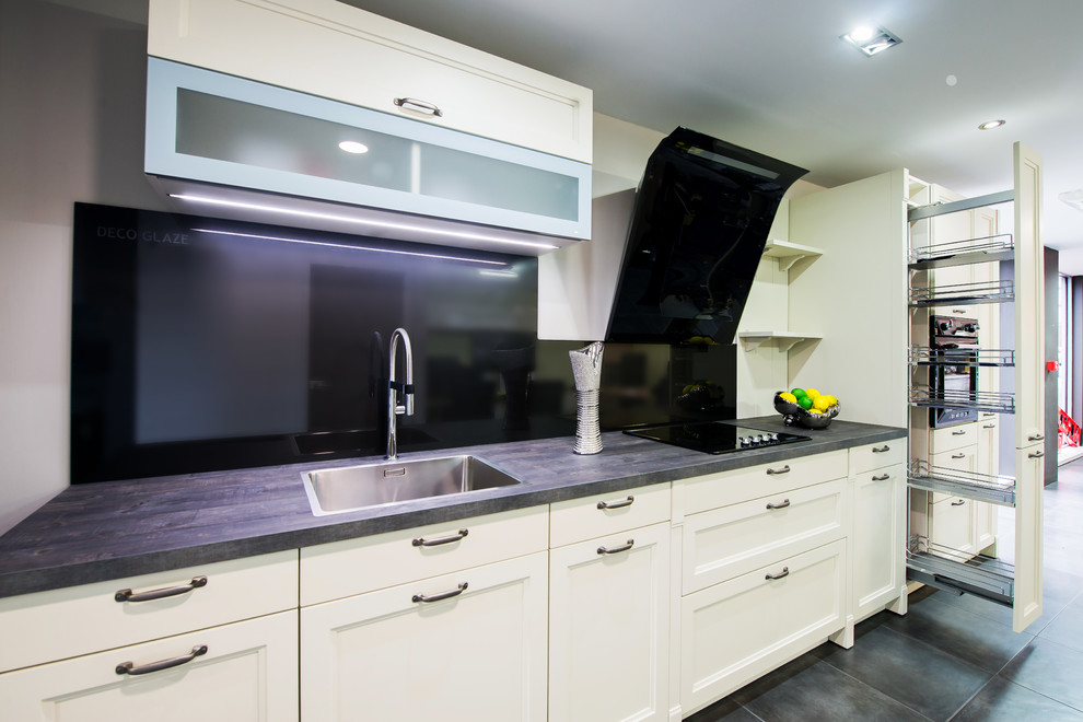 Lantlig inredning av ett linjärt kök med öppen planlösning, med en enkel diskho, skåp i shakerstil, beige skåp, laminatbänkskiva, stänkskydd med metallisk yta, glaspanel som stänkskydd och svarta vitvaror