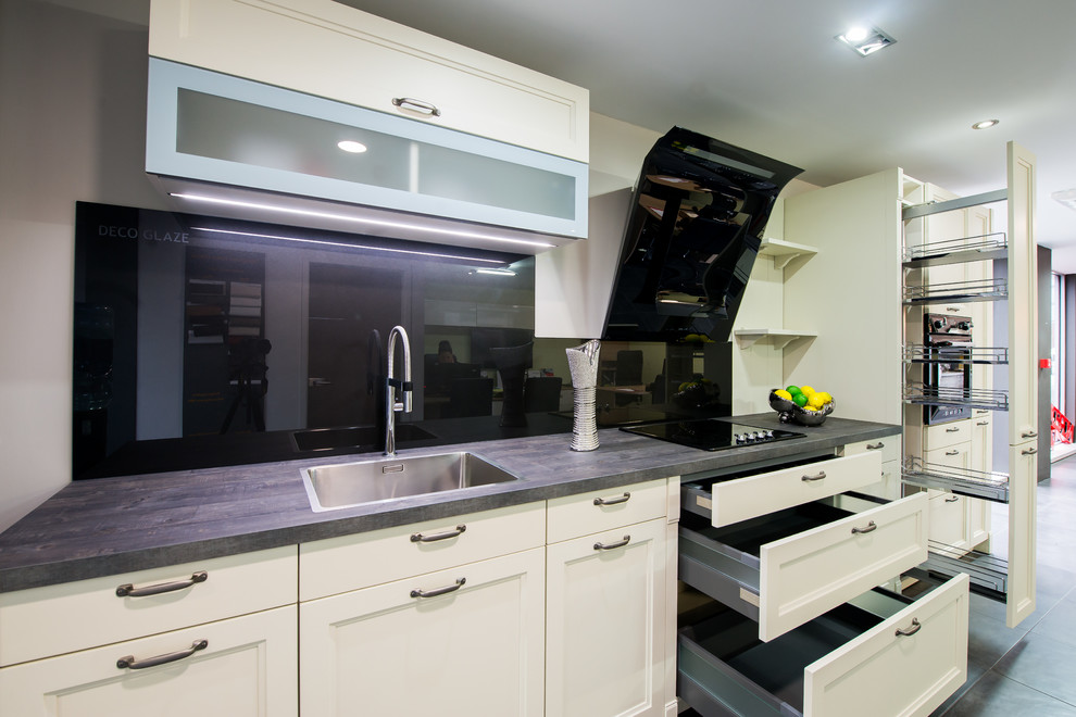 This is an example of a farmhouse grey and cream single-wall open plan kitchen in London with shaker cabinets, beige cabinets, laminate countertops, metallic splashback, glass sheet splashback and black appliances.