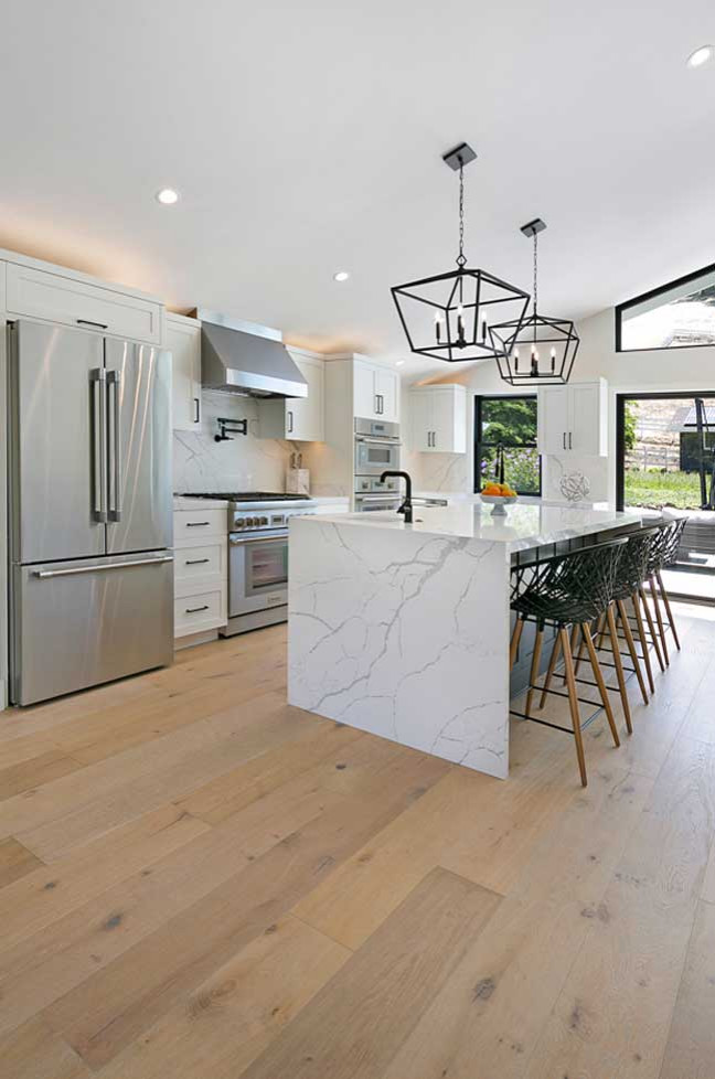 Open concept kitchen - large contemporary single-wall light wood floor, beige floor and vaulted ceiling open concept kitchen idea in San Francisco with recessed-panel cabinets, white cabinets, quartz countertops, white backsplash, quartz backsplash, stainless steel appliances, an island, white countertops and a farmhouse sink