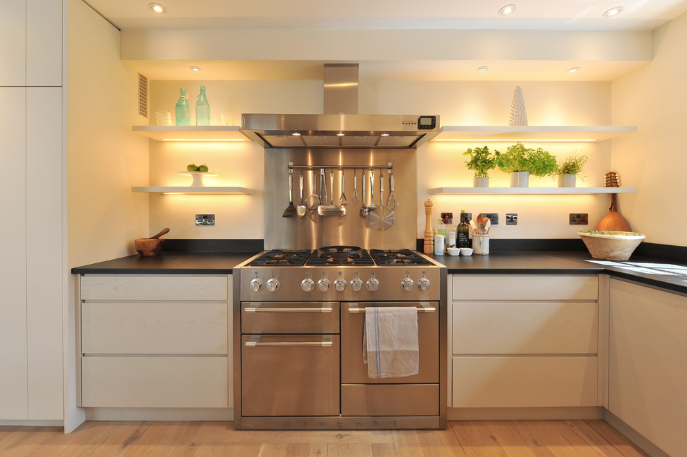 Moderne Küche mit flächenbündigen Schrankfronten, beigen Schränken, Küchengeräten aus Edelstahl und hellem Holzboden in Hampshire