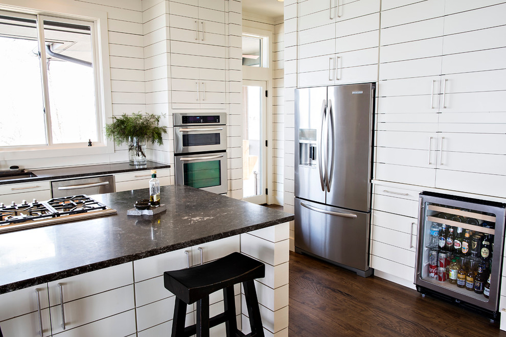 Lantlig inredning av ett mellanstort kök, med en undermonterad diskho, släta luckor, vita skåp, granitbänkskiva, rostfria vitvaror, mörkt trägolv, en köksö och brunt golv