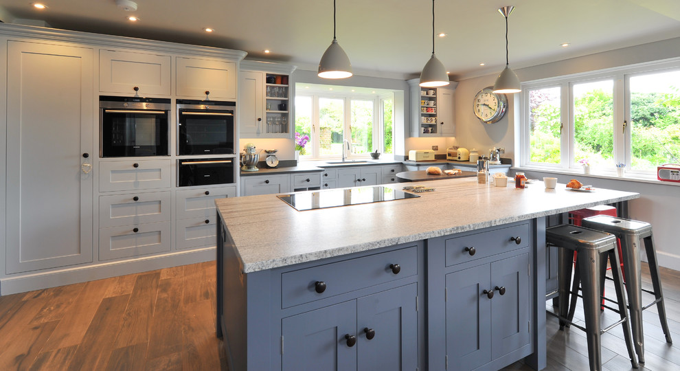 This is an example of a large contemporary open plan kitchen in Hampshire with a built-in sink, blue cabinets, granite worktops, black appliances, ceramic flooring and an island.