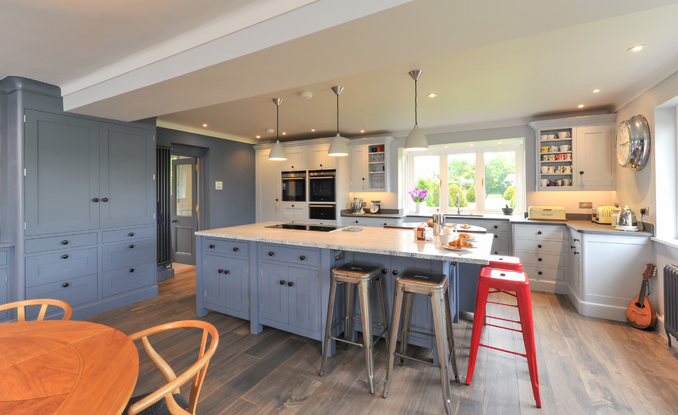 Photo of a large contemporary open plan kitchen in Hampshire with a built-in sink, blue cabinets, granite worktops, black appliances, ceramic flooring and an island.