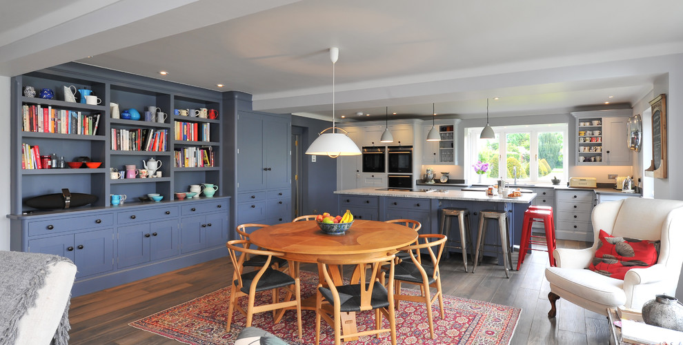 Пример оригинального дизайна: большая кухня-гостиная в стиле неоклассика (современная классика) с синими фасадами, гранитной столешницей и островом
