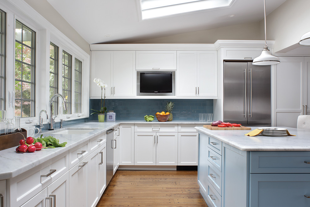 Cette image montre une grande cuisine américaine traditionnelle en U avec un placard à porte shaker, des portes de placard blanches, une crédence bleue, un électroménager en acier inoxydable, parquet clair et îlot.