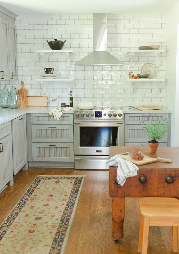 Exempel på ett klassiskt kök, med en nedsänkt diskho, luckor med upphöjd panel, grå skåp, bänkskiva i kvartsit, stänkskydd i tunnelbanekakel, rostfria vitvaror, ljust trägolv och en köksö