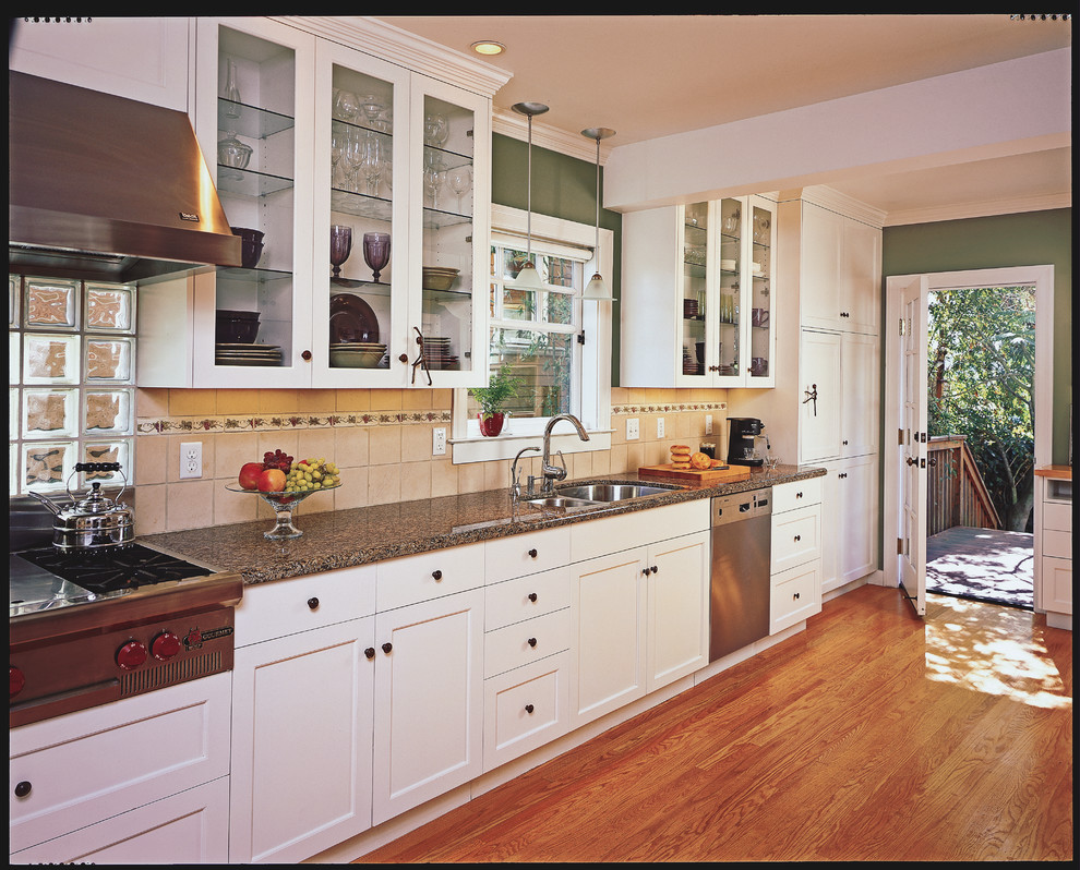 Inredning av ett amerikanskt mellanstort kök, med en undermonterad diskho, skåp i shakerstil, vita skåp, granitbänkskiva, rostfria vitvaror och mellanmörkt trägolv
