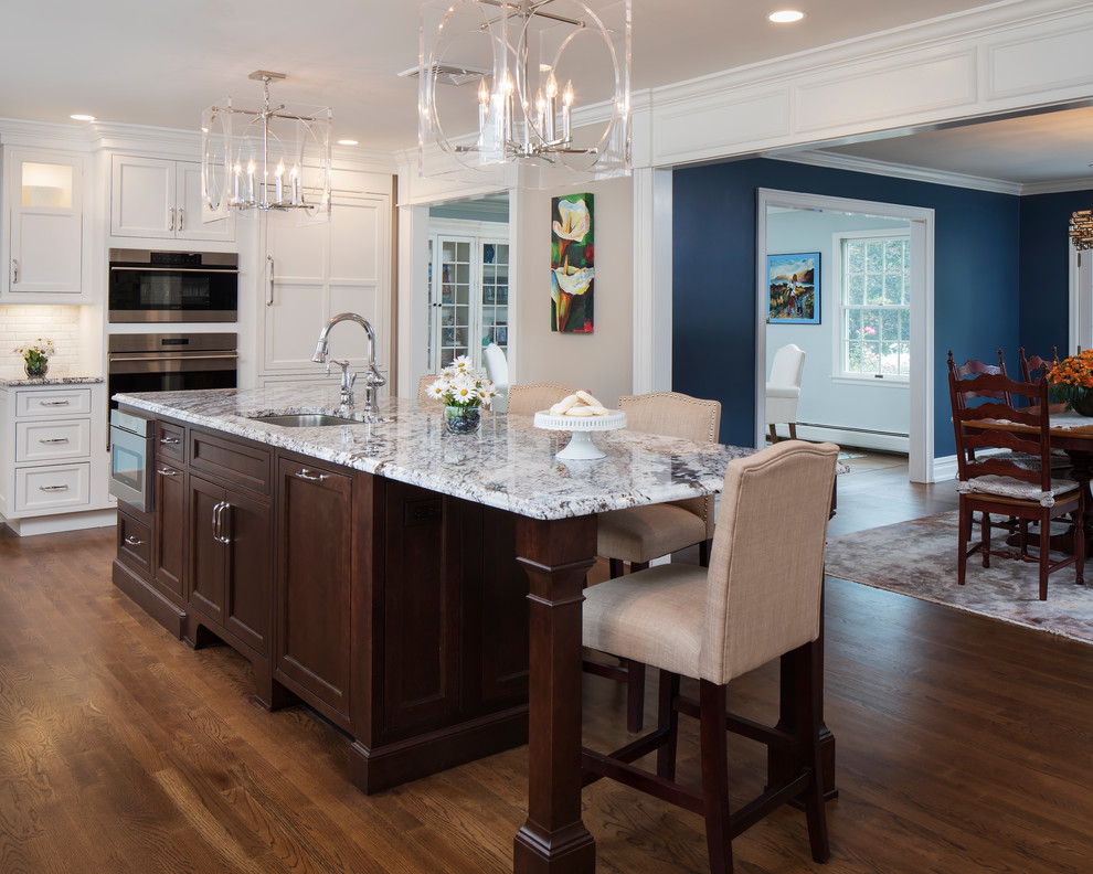 Example of a mid-sized classic l-shaped medium tone wood floor and brown floor eat-in kitchen design in New York with an undermount sink, shaker cabinets, white cabinets, quartz countertops, white backsplash, subway tile backsplash, stainless steel appliances, an island and gray countertops
