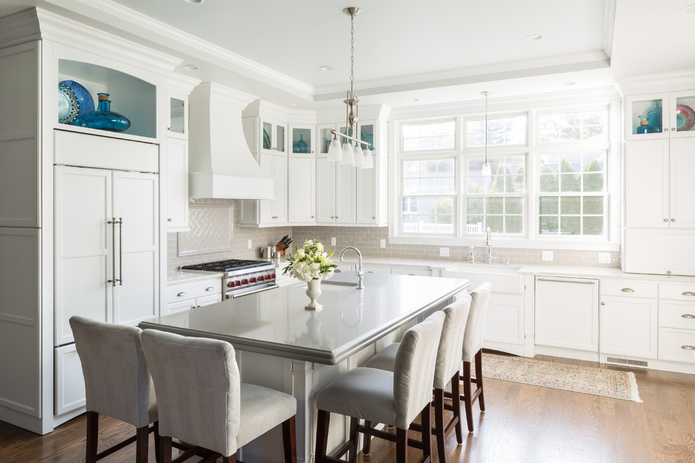 Eat-in kitchen - large transitional l-shaped dark wood floor and brown floor eat-in kitchen idea in Providence with a farmhouse sink, recessed-panel cabinets, white cabinets, quartz countertops, gray backsplash, subway tile backsplash, paneled appliances and an island