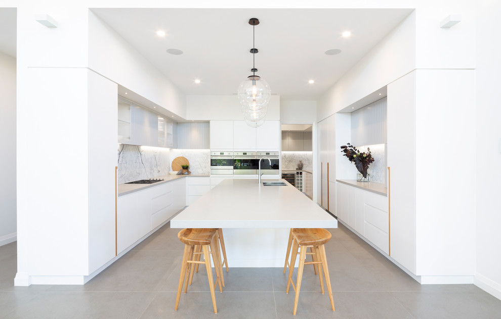 Foto på ett funkis vit u-kök, med en dubbel diskho, släta luckor, vita skåp, grått stänkskydd, rostfria vitvaror, en köksö och grått golv