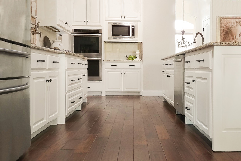 Idéer för ett stort klassiskt kök, med luckor med upphöjd panel, vita skåp, granitbänkskiva, beige stänkskydd, rostfria vitvaror, mörkt trägolv, en köksö och brunt golv
