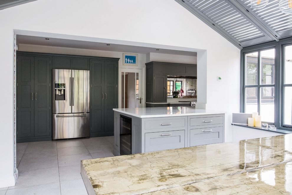 Inspiration for a medium sized contemporary galley kitchen/diner in Kent with an integrated sink, recessed-panel cabinets, grey cabinets, quartz worktops, metallic splashback, glass tiled splashback, stainless steel appliances, limestone flooring, an island and beige floors.
