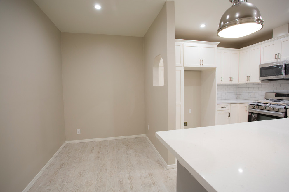 Medium sized traditional single-wall open plan kitchen in Los Angeles with a belfast sink, shaker cabinets, white cabinets, quartz worktops, white splashback, metro tiled splashback, stainless steel appliances, porcelain flooring, an island, beige floors and white worktops.