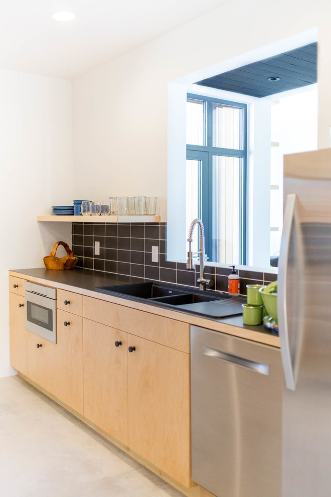 Example of a mid-sized minimalist galley concrete floor enclosed kitchen design in Other with an undermount sink, flat-panel cabinets, light wood cabinets, solid surface countertops, black backsplash, subway tile backsplash, stainless steel appliances and no island