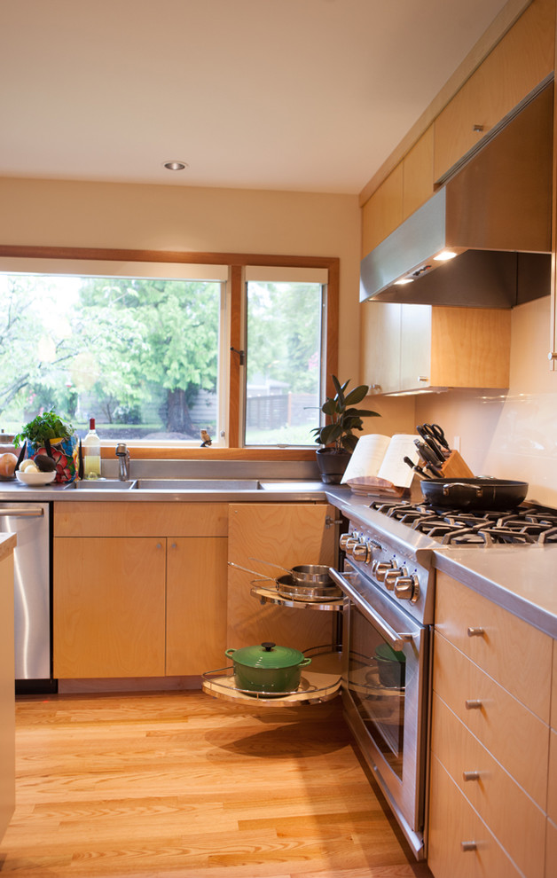 Foto di una grande cucina moderna con lavello integrato, ante lisce, ante in legno chiaro, top in acciaio inossidabile, paraspruzzi bianco, paraspruzzi con piastrelle in ceramica, elettrodomestici in acciaio inossidabile e parquet chiaro