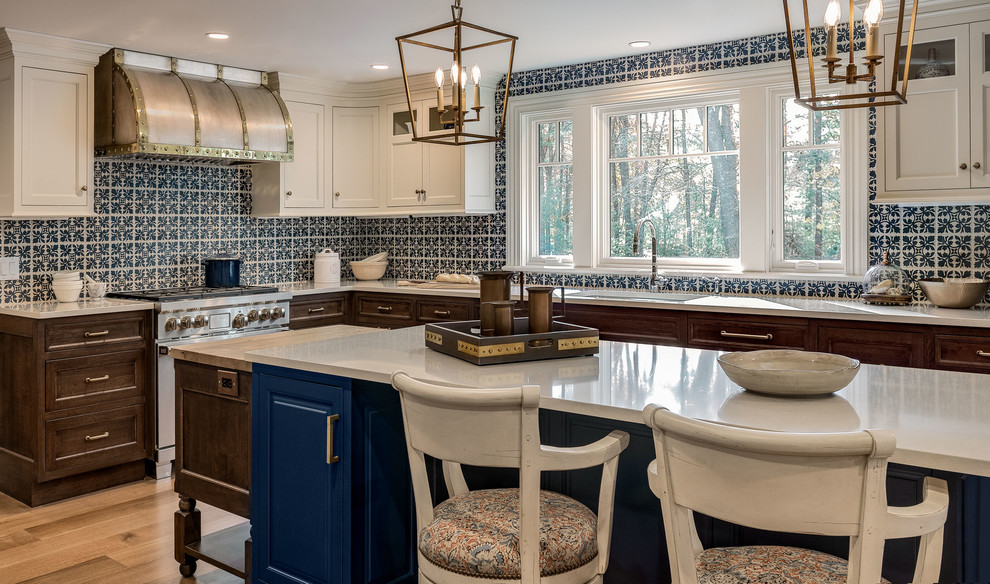 Inredning av ett klassiskt avskilt, stort vit vitt l-kök, med en undermonterad diskho, luckor med infälld panel, blå skåp, bänkskiva i kvarts, blått stänkskydd, stänkskydd i keramik, integrerade vitvaror, mellanmörkt trägolv, en köksö och brunt golv