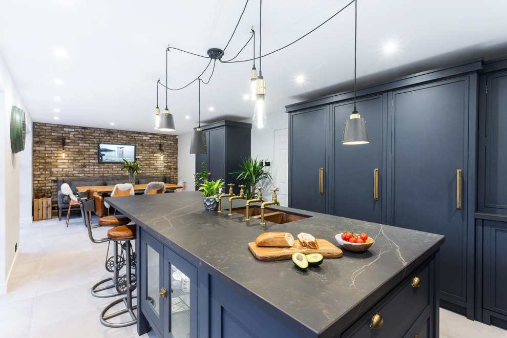 This is an example of a large urban l-shaped kitchen/diner in Essex with a double-bowl sink, shaker cabinets, blue cabinets, composite countertops, multi-coloured splashback, ceramic splashback, black appliances, porcelain flooring, an island, grey floors and black worktops.
