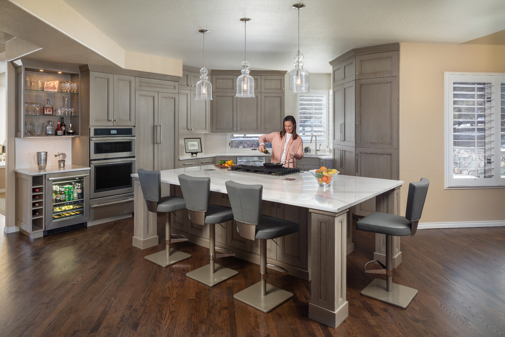 This is an example of a large traditional single-wall kitchen/diner in Denver with a submerged sink, shaker cabinets, grey cabinets, engineered stone countertops, white splashback, ceramic splashback, integrated appliances, medium hardwood flooring, an island, brown floors and white worktops.