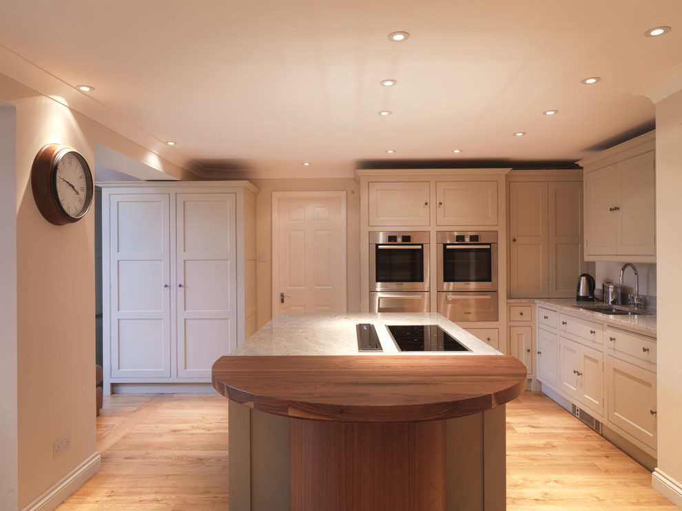 Medium sized classic l-shaped open plan kitchen in Hampshire with a built-in sink, shaker cabinets, beige cabinets, granite worktops, stainless steel appliances, light hardwood flooring and an island.
