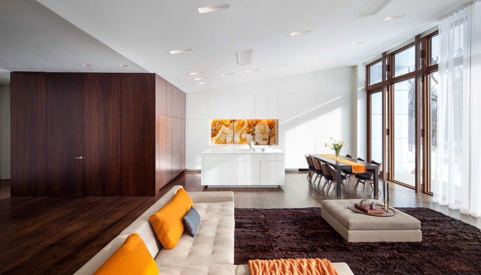 Идея дизайна: кухня-гостиная в стиле модернизм с плоскими фасадами, белыми фасадами, оранжевым фартуком, фартуком из каменной плиты и техникой под мебельный фасад