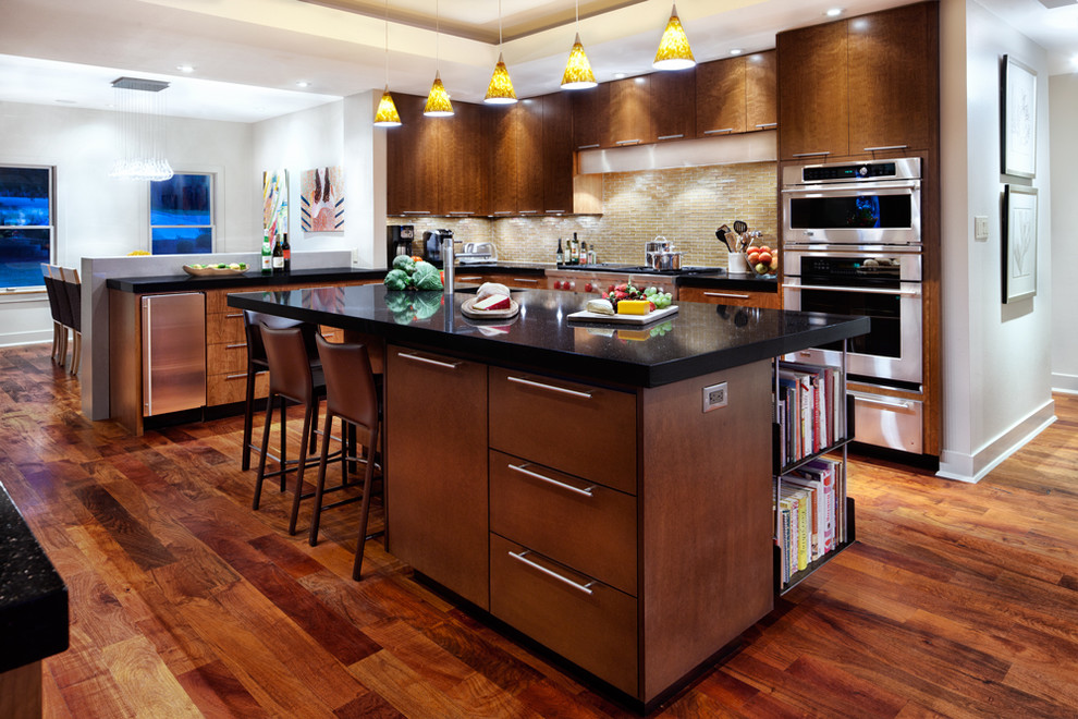 Example of a trendy medium tone wood floor kitchen design in Austin with flat-panel cabinets, medium tone wood cabinets, granite countertops, beige backsplash, glass tile backsplash, stainless steel appliances and an island