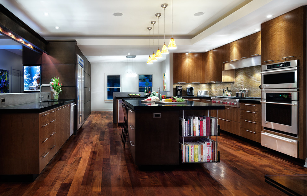 Moderne Küche mit flächenbündigen Schrankfronten, hellbraunen Holzschränken, Granit-Arbeitsplatte, Küchenrückwand in Beige, Rückwand aus Glasfliesen, Küchengeräten aus Edelstahl, braunem Holzboden und Kücheninsel in Austin