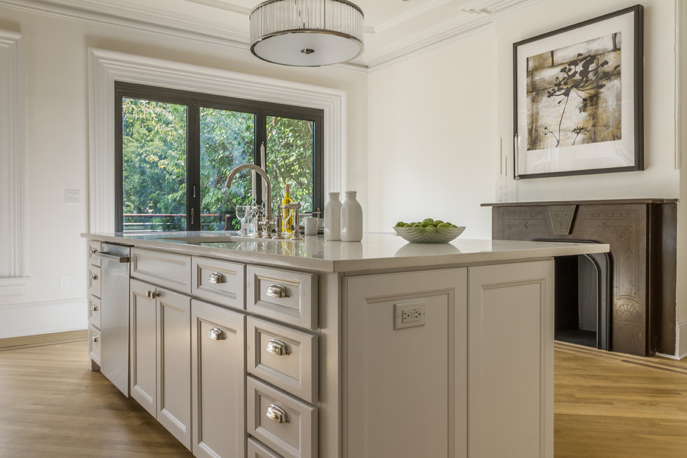Exempel på ett mellanstort klassiskt kök, med en undermonterad diskho, luckor med infälld panel, vita skåp, bänkskiva i kvarts, vitt stänkskydd, stänkskydd i porslinskakel, rostfria vitvaror, mellanmörkt trägolv, en köksö och beiget golv