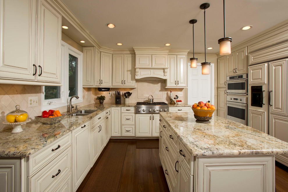 Exempel på ett stort klassiskt kök, med en dubbel diskho, luckor med upphöjd panel, beige stänkskydd, integrerade vitvaror, granitbänkskiva, stänkskydd i stenkakel, en köksö, beige skåp och mörkt trägolv