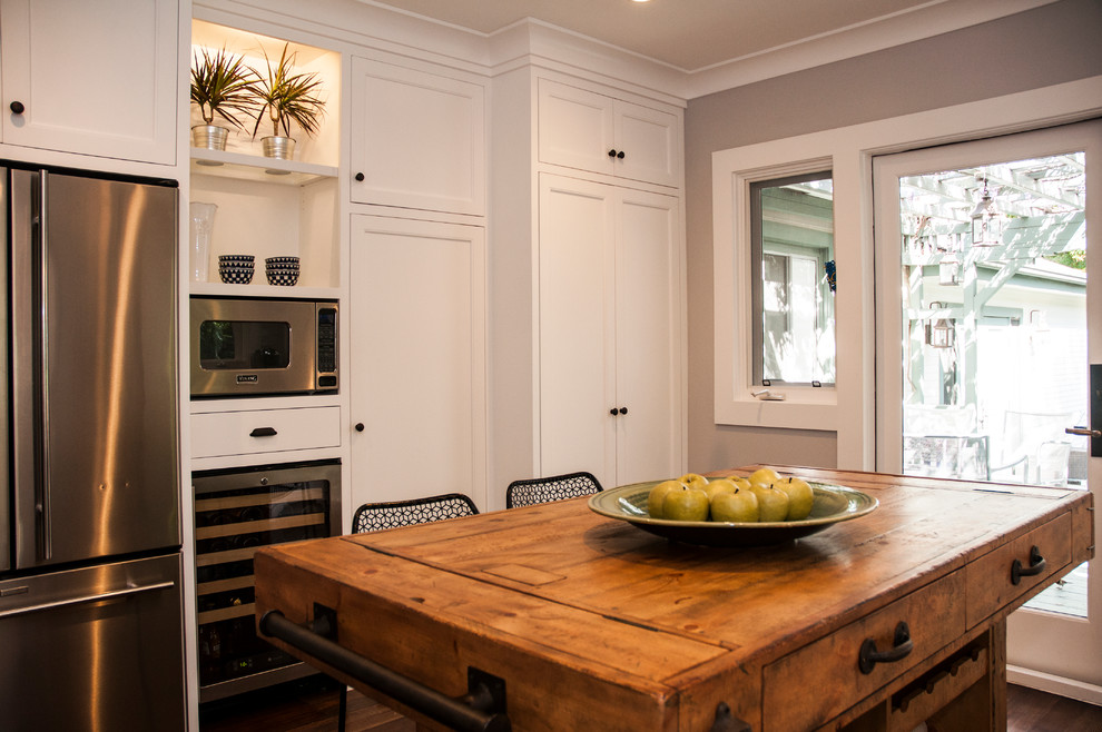Inspiration for a mid-sized eclectic u-shaped dark wood floor and brown floor enclosed kitchen remodel in Los Angeles with a farmhouse sink, shaker cabinets, white cabinets, quartz countertops, white backsplash, subway tile backsplash, stainless steel appliances and an island