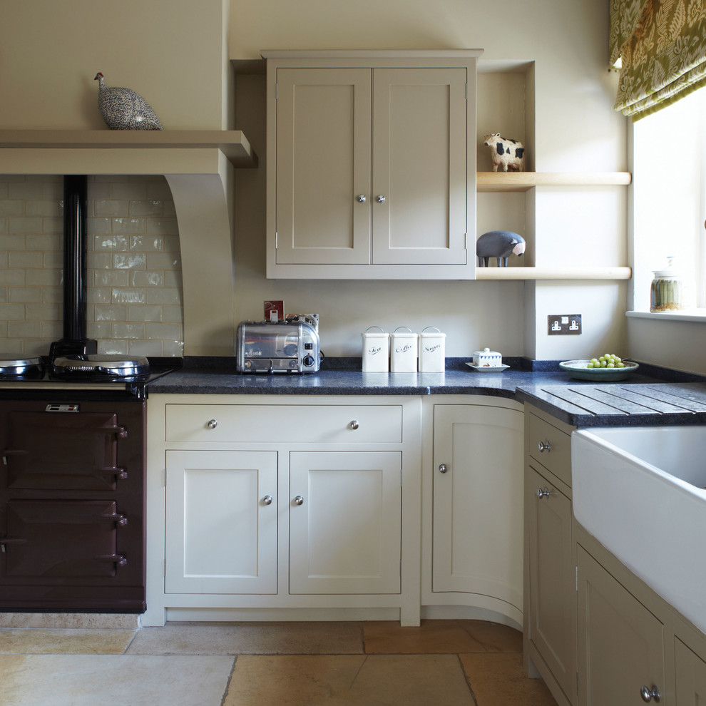 Inspiration for a country l-shaped kitchen in Dorset with a belfast sink, shaker cabinets, beige cabinets, white splashback, metro tiled splashback, black appliances and beige floors.