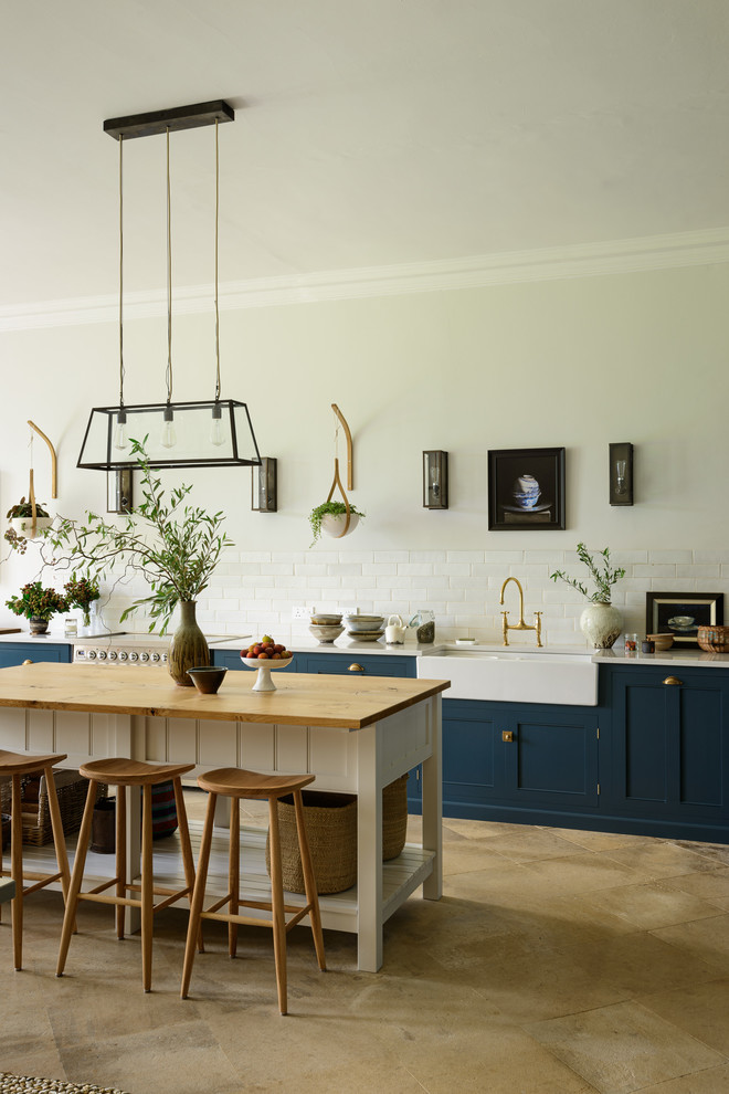 Klassische Küche mit Landhausspüle, Schrankfronten im Shaker-Stil, blauen Schränken, Küchenrückwand in Weiß, Rückwand aus Metrofliesen, Kücheninsel, beigem Boden und weißer Arbeitsplatte in Sonstige