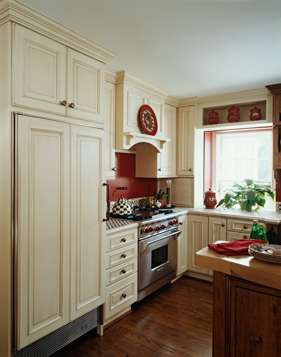 他の地域にあるカントリー風のおしゃれなキッチン (エプロンフロントシンク、レイズドパネル扉のキャビネット、タイルカウンター、赤いキッチンパネル、パネルと同色の調理設備、無垢フローリング) の写真