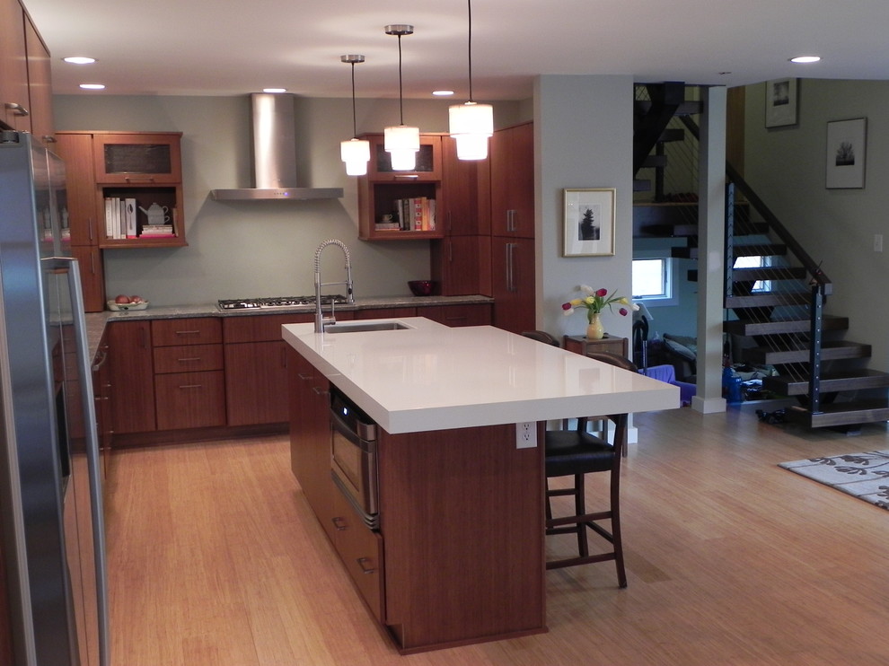 Modern inredning av ett stort kök, med en dubbel diskho, släta luckor, skåp i mellenmörkt trä, bänkskiva i kvartsit, rostfria vitvaror, ljust trägolv, en köksö och beiget golv