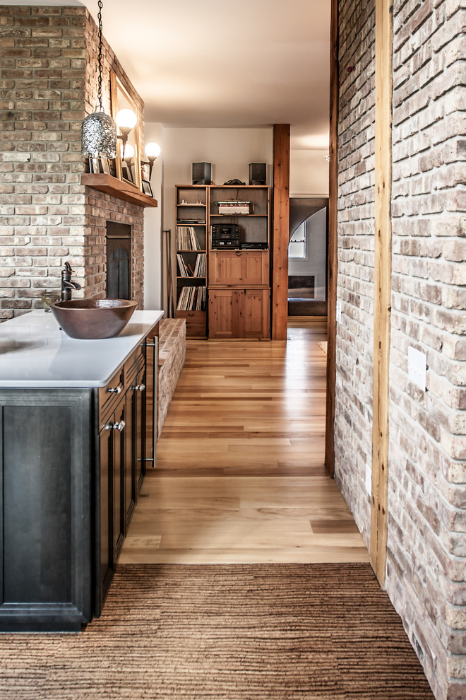 Große Stilmix Küche mit Schrankfronten mit vertiefter Füllung, schwarzen Schränken, braunem Boden, Rückwand aus Backstein, hellem Holzboden und Kücheninsel in Sonstige